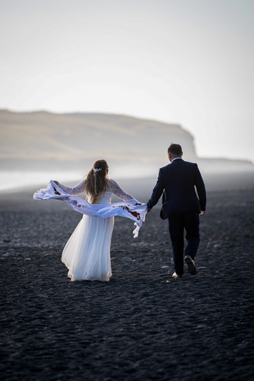 Couple running together on a black sand beach